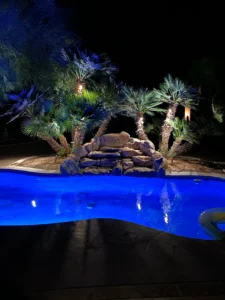 Beautiful lighting for a pool at night with palm trees and stones.